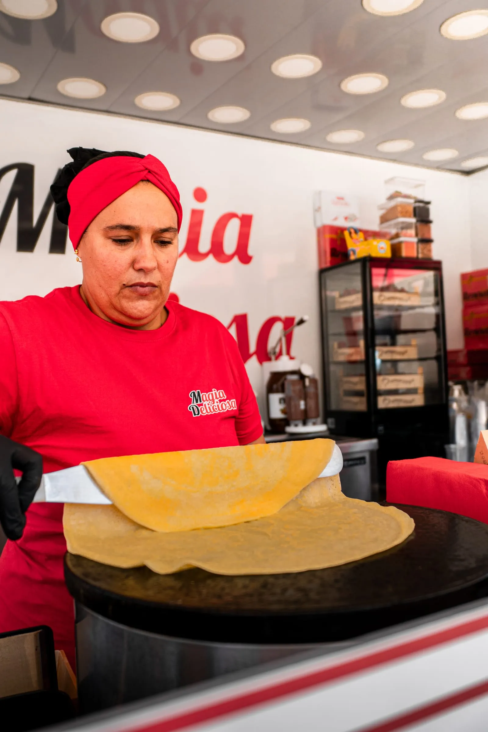 Empregada de farda vermelha estende um crepe acabado de fazer no balcão da roulotte.