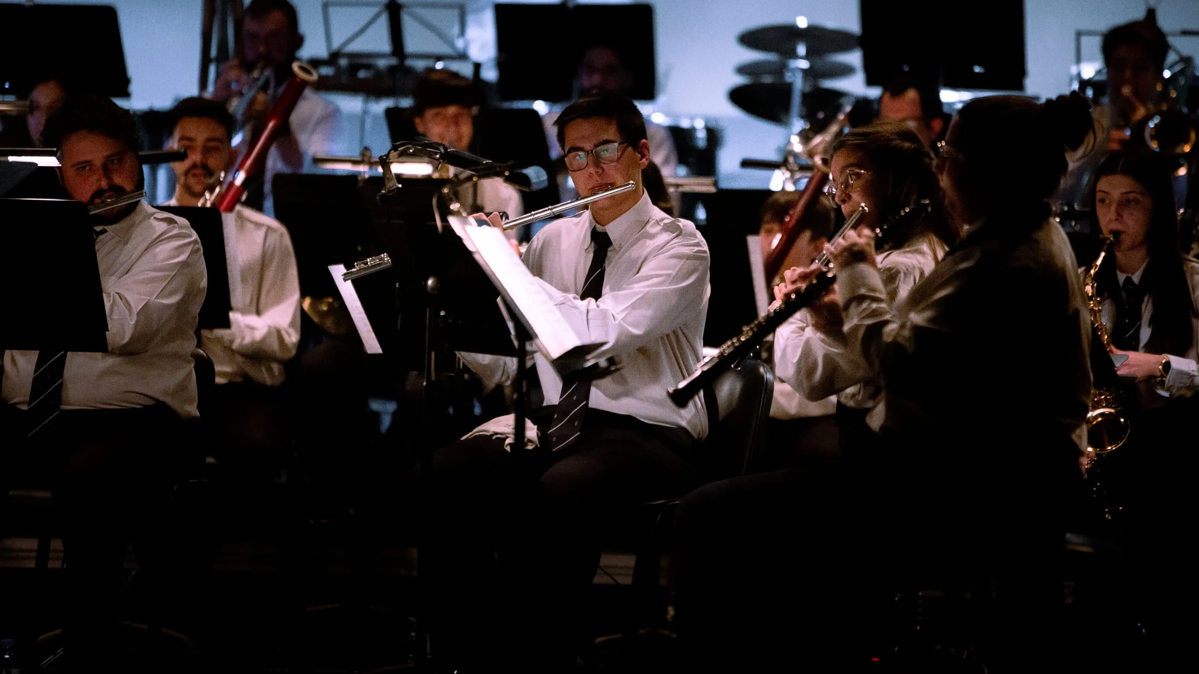 Orquestra a tocar, vista de frente, com os atris iluminados.