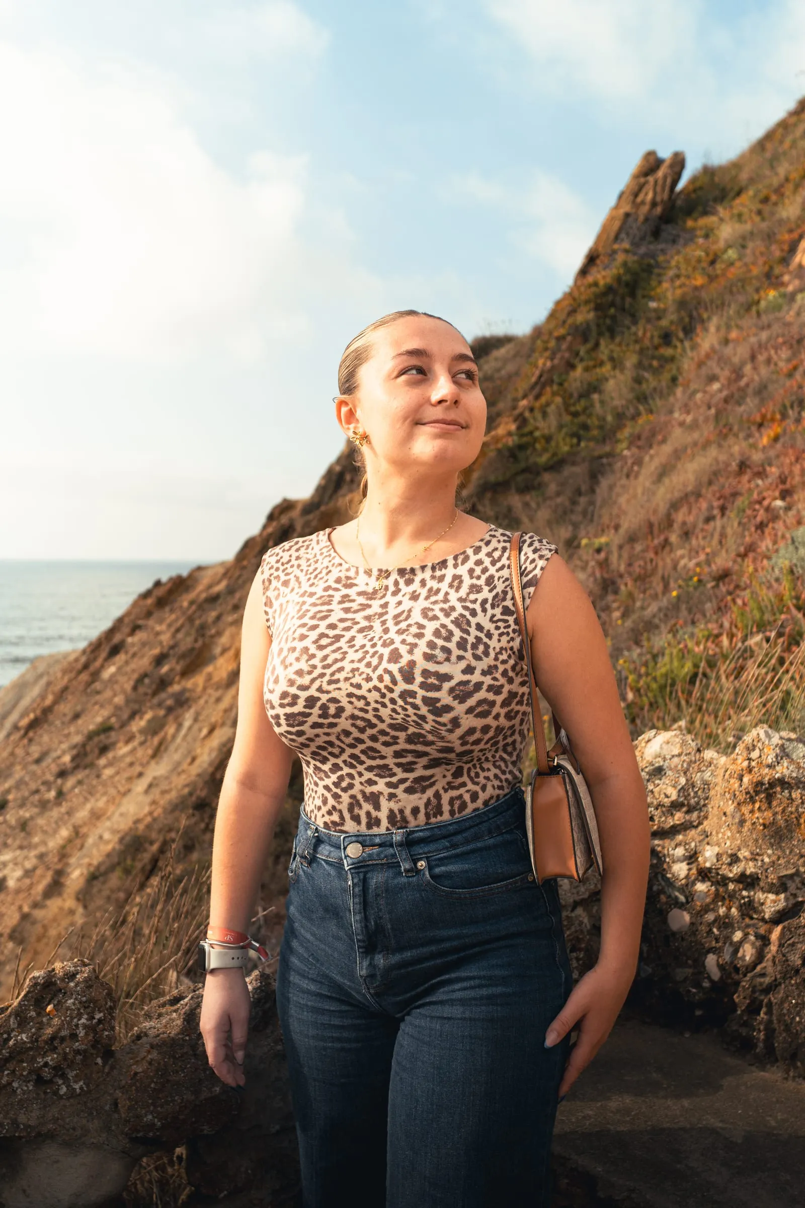Retrato de mulher ao pôr do sol, com a arriba e o mar atrás.